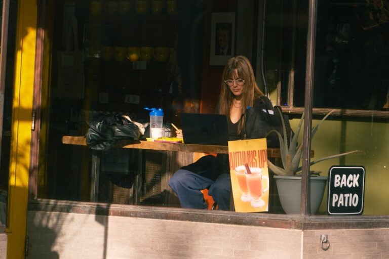 Woman working on laptop at outdoor cafe table.