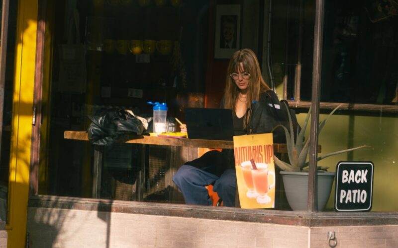 Woman working on laptop at outdoor cafe table.