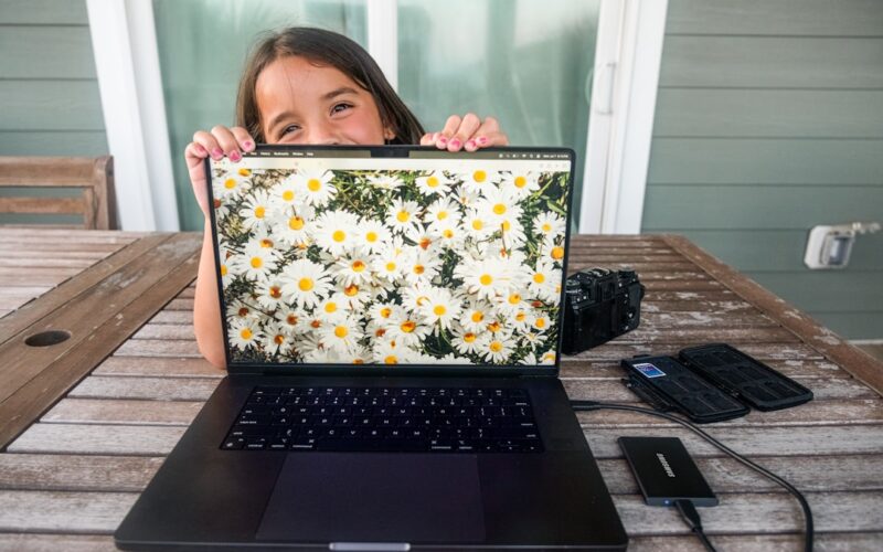 Girl peeking over laptop displaying daisies