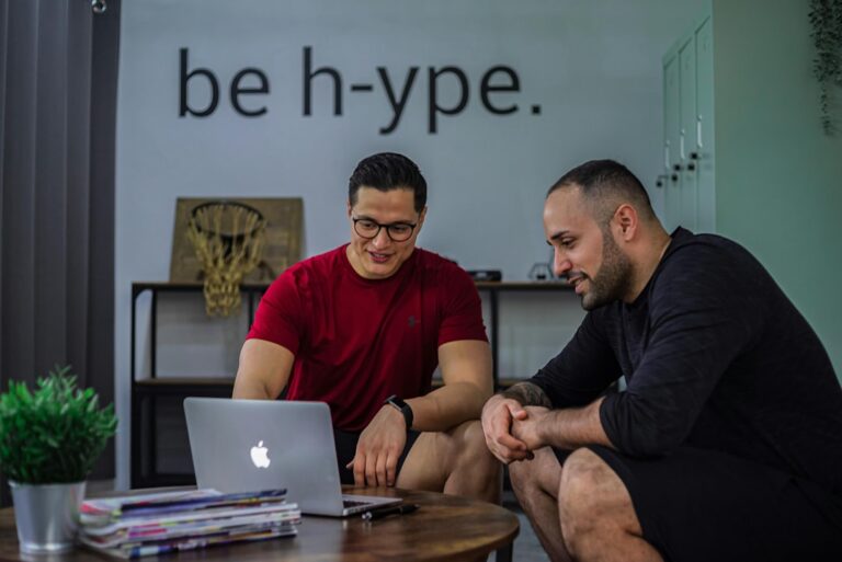 Two men sitting on a coffee table looking at a laptop