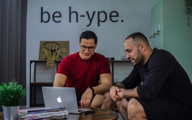 Two men sitting on a coffee table looking at a laptop